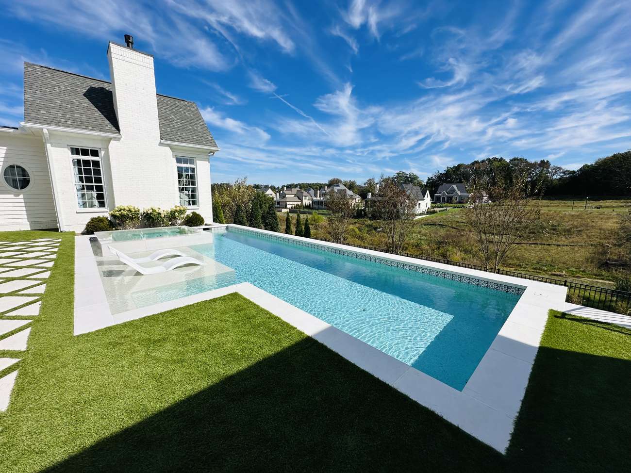 Geometric pool and manicured lawn beside a white modern home