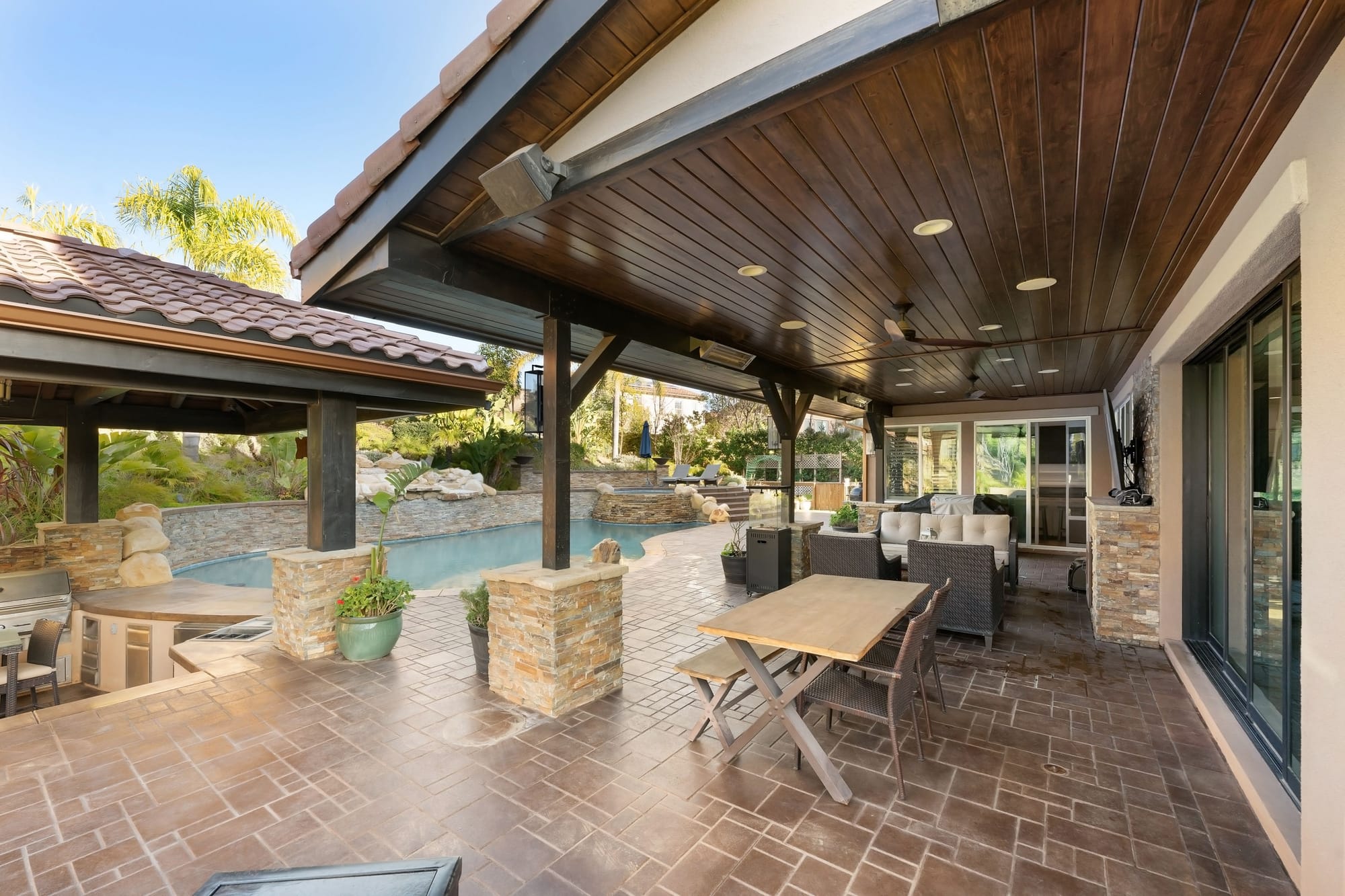 Covered patio with stone columns beside a pool