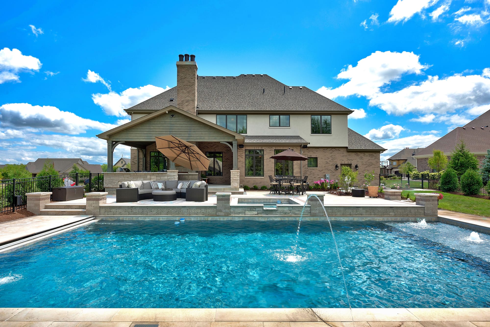 Backyard pool with fountains in front of a large home